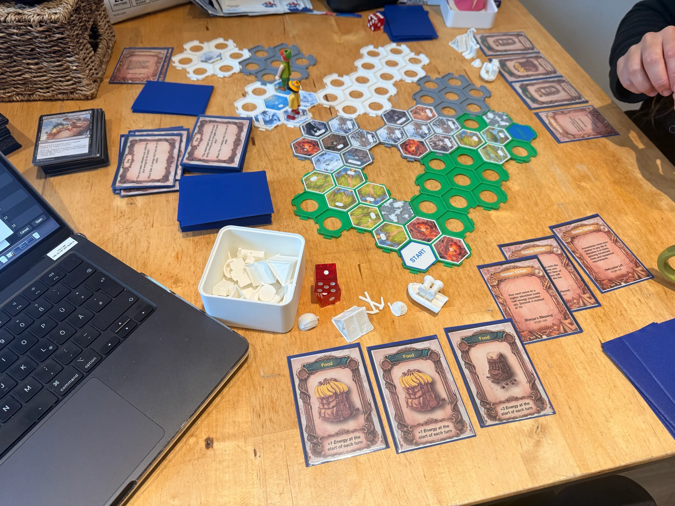 The table from above: half-built mountain, decks of Day, Food and Golden Ticket cards, 3D-printed gear tokens and red dice.